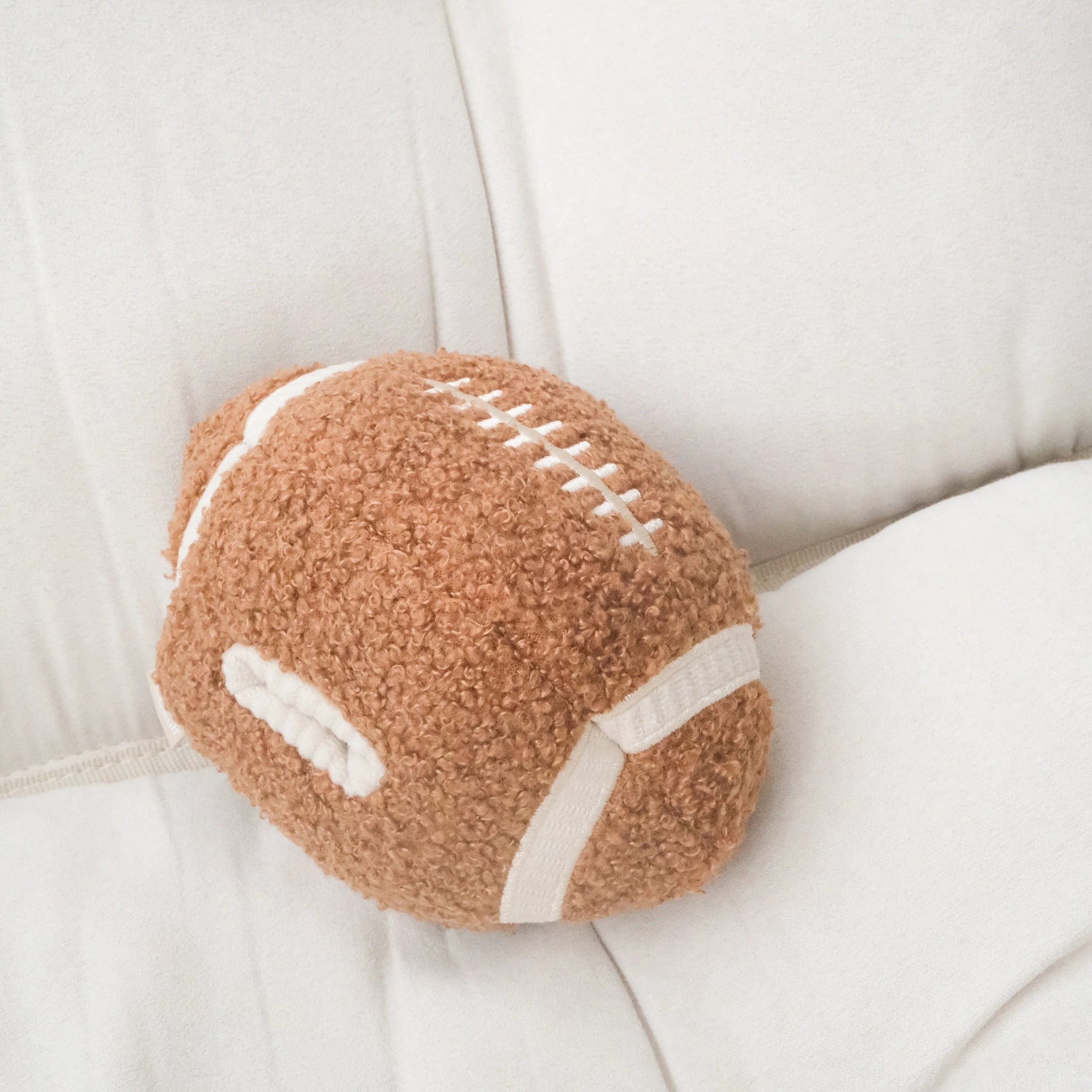 Lambwolf Collective Football plush dog toy displayed on a white sofa