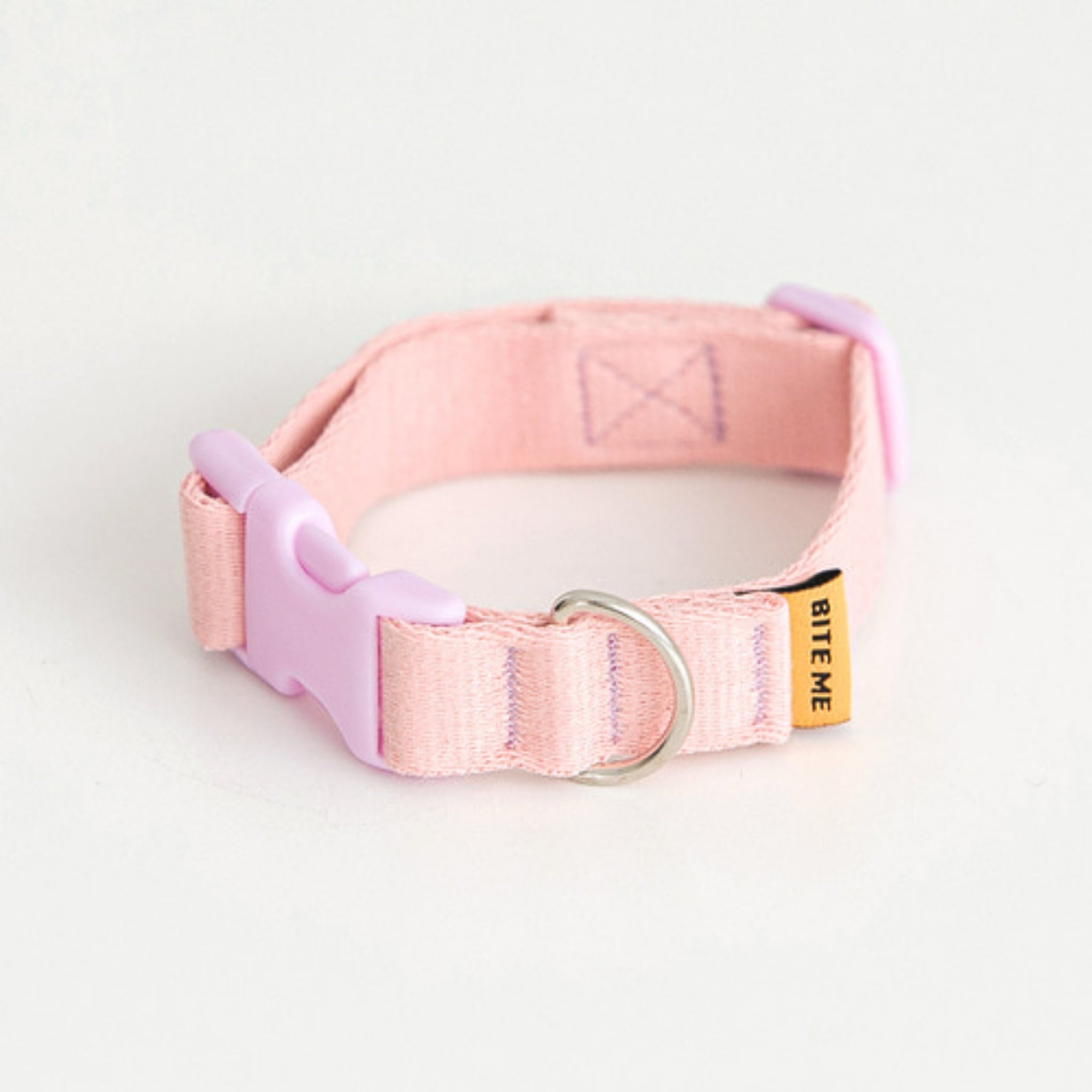 A high-quality studio shot of the pastel light pink Bite Me Candy Crayon dog collar, featuring its contrasting lavender quick-release curved buckle and silver metal D-ring.