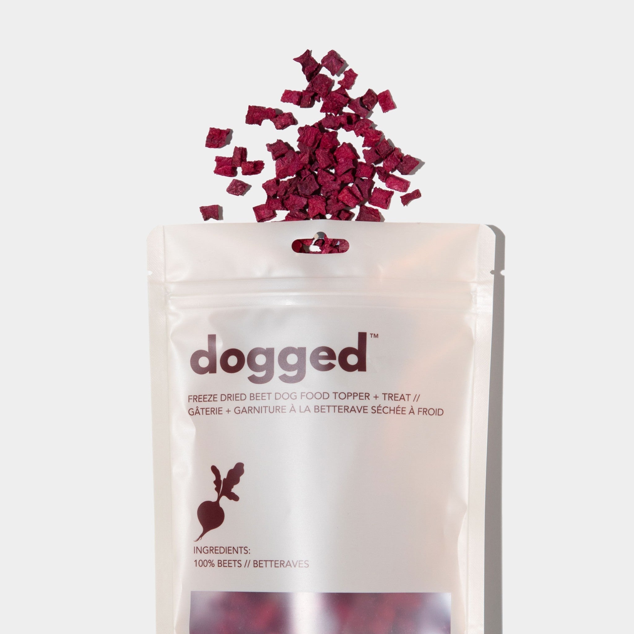 A flat lay view of a white stand-up pouch for Dogged freeze-dried beet dog food topper and treat, featuring rich burgundy-red dried beet pieces scattered neatly just above the top opening.