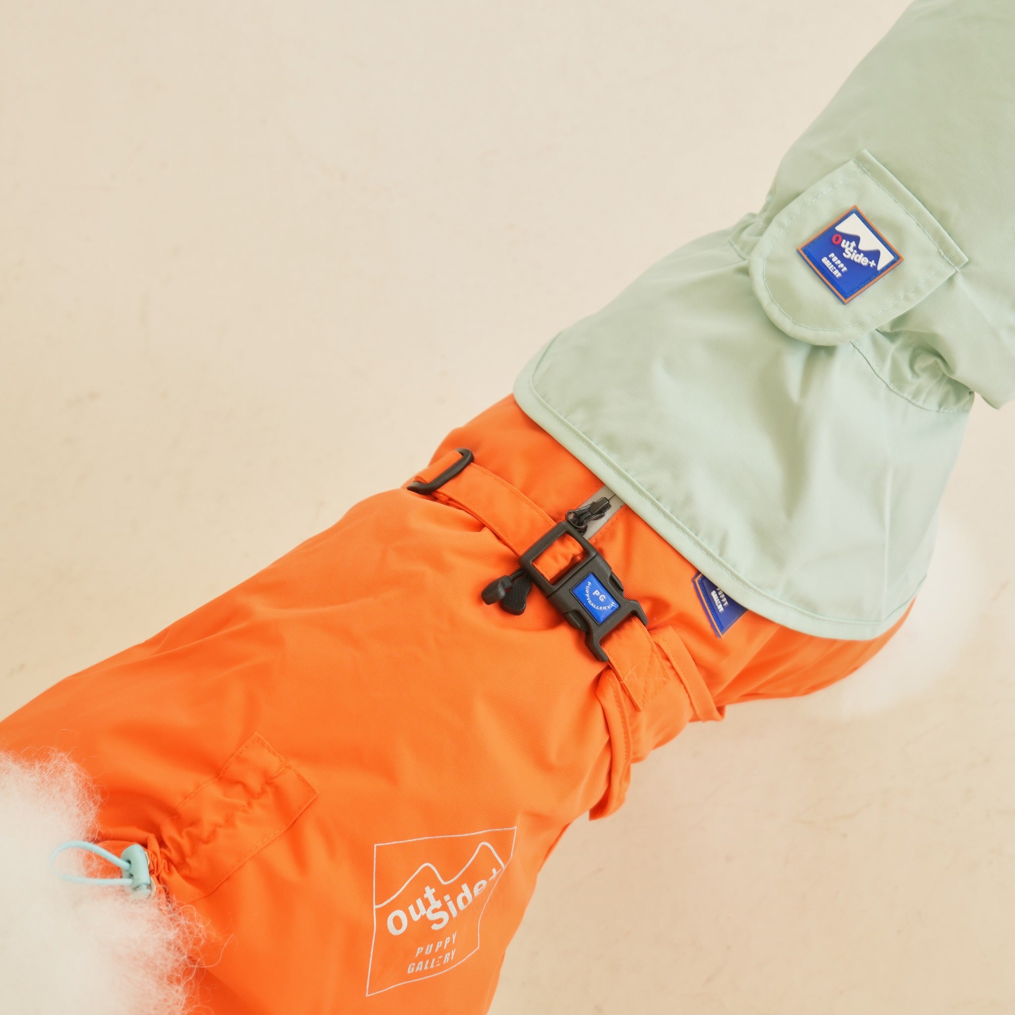 Close-up view of the back of the orange dog raincoat, showing the adjustable black buckle strap and connection point for the mint green poncho hood.