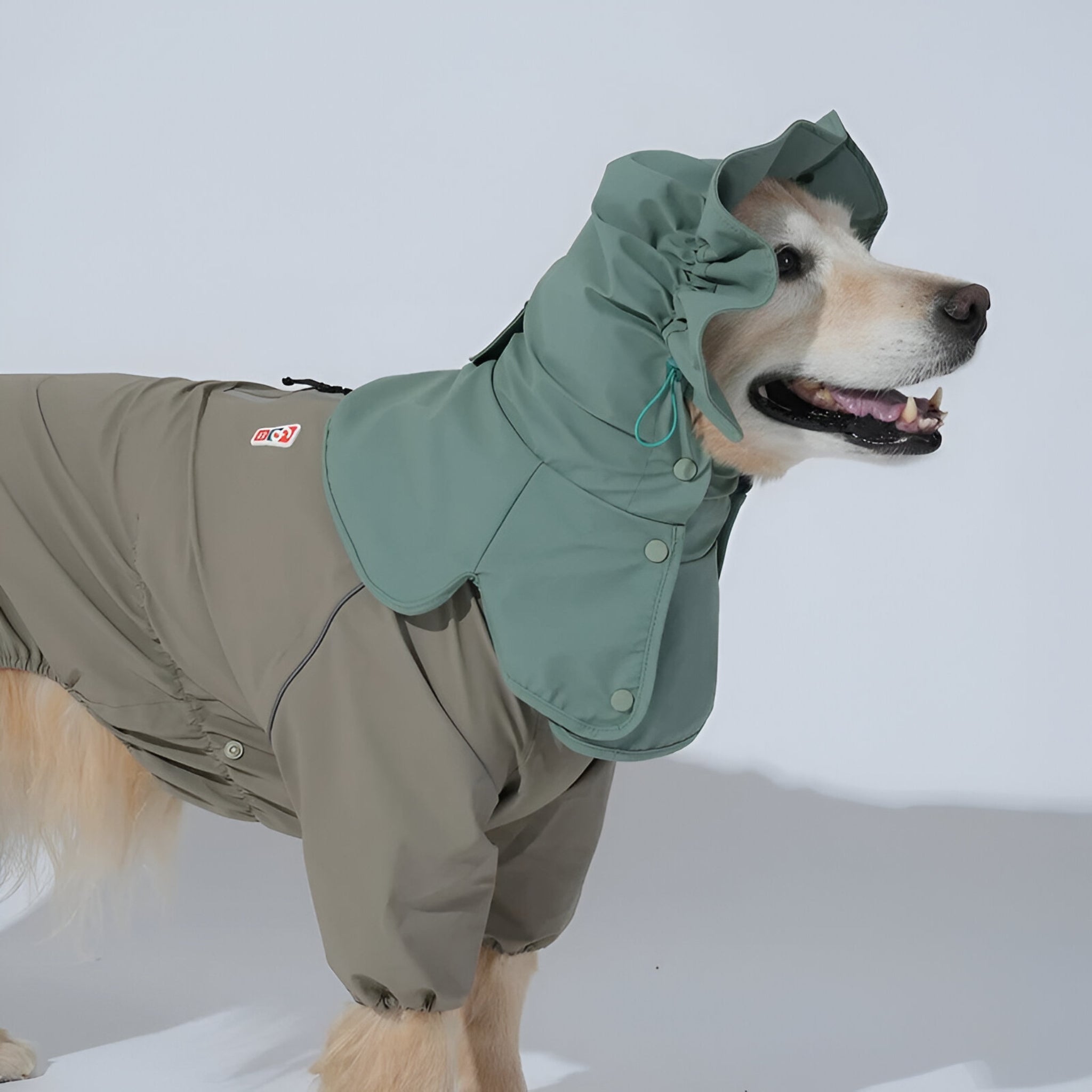 Side profile view of a large light-colored dog standing against a plain white background, showcasing the full head and neck coverage of the khaki green protective dog rain snood.