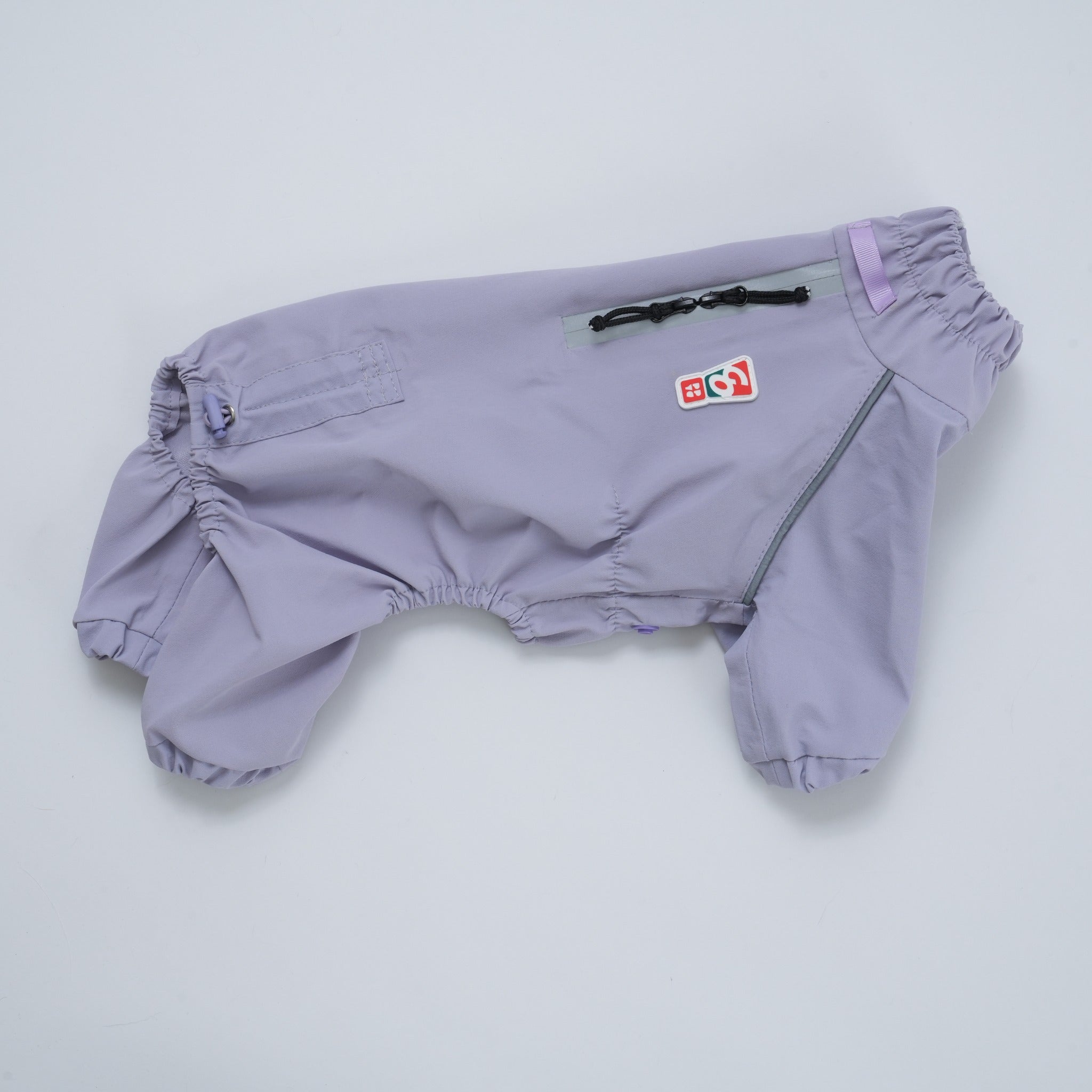 A flatlay studio product shot displaying the lavender Puppy Gallery Go Pro Weather Suit, highlighting the waterproof zipper closure, functional harness hole, and signature logo patch.