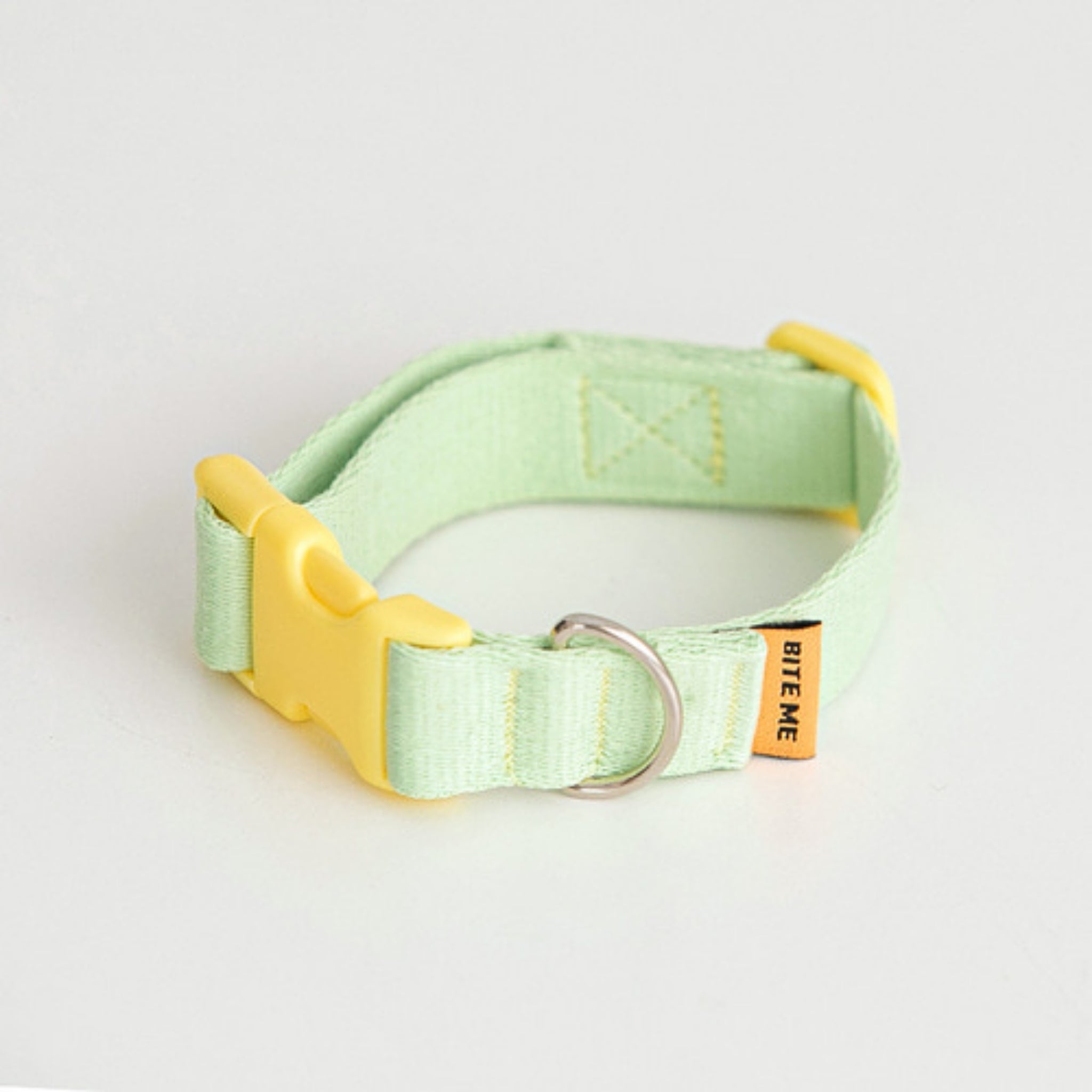 A studio product photo of the pastel light green Bite Me Candy Crayon dog collar, showcasing the bright yellow quick-release plastic buckle and stitched canvas details.