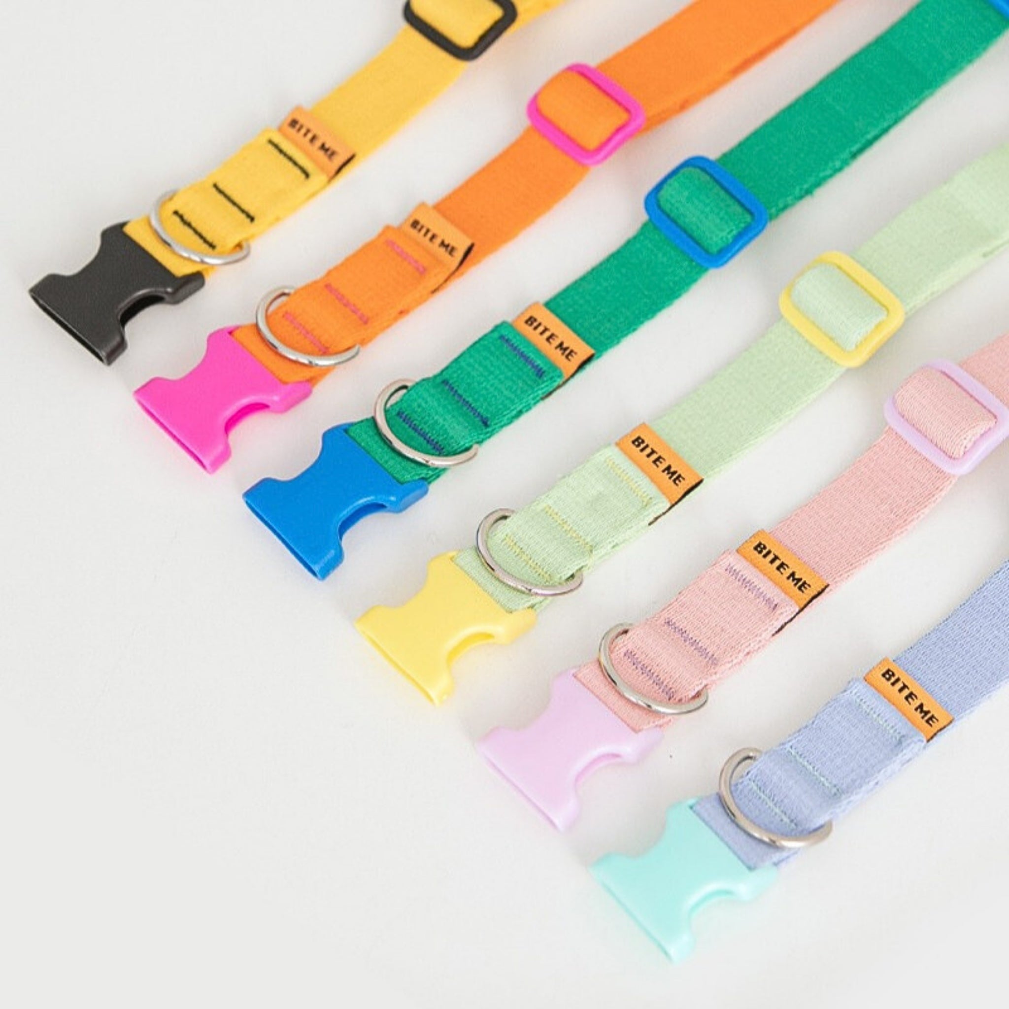 A top-down diagonal layout showcasing the full color collection of Bite Me Candy Crayon dog collars, displaying the vibrant mix-and-match combinations of pastel straps and colorful ergonomic plastic buckles.