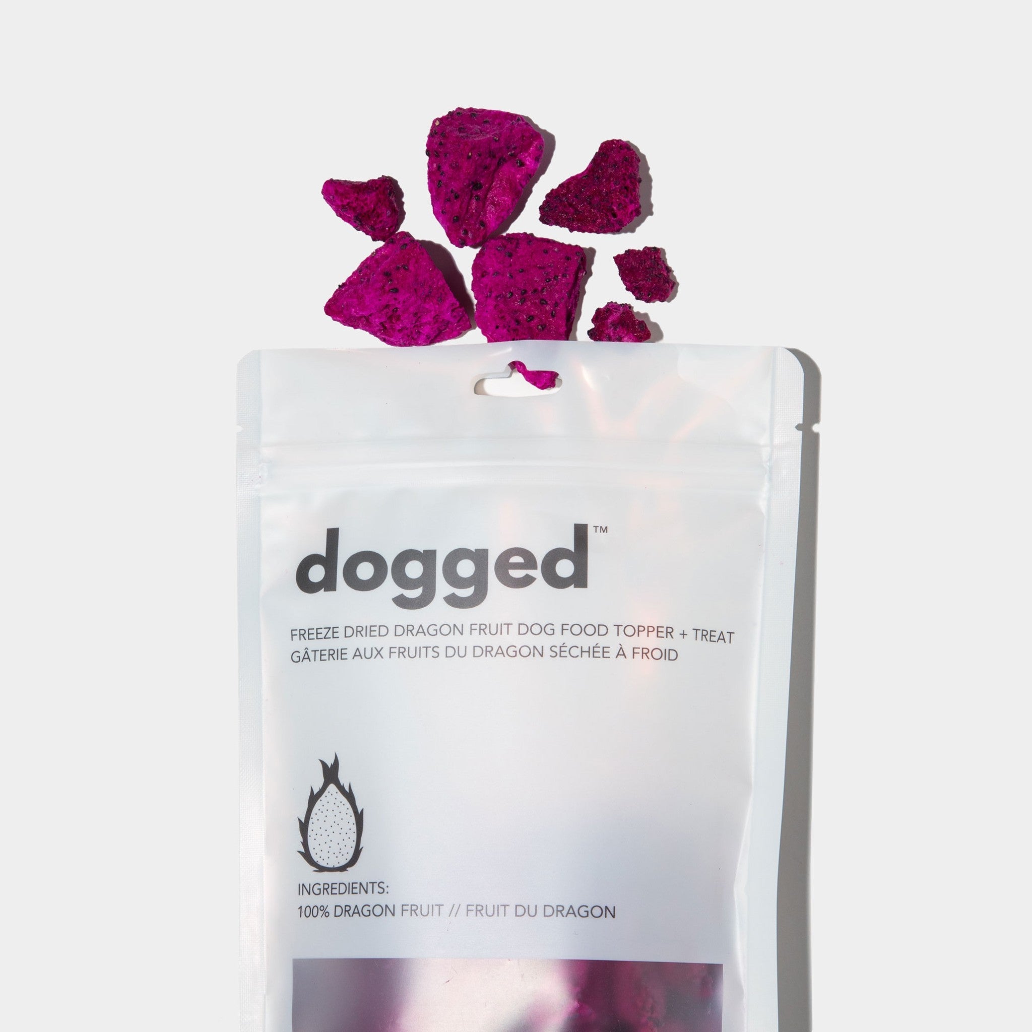 A flat lay view of a white stand-up pouch for Dogged freeze-dried dragon fruit dog food topper and treat, featuring vibrant magenta-pink dragon fruit pieces arranged neatly just above the package opening.