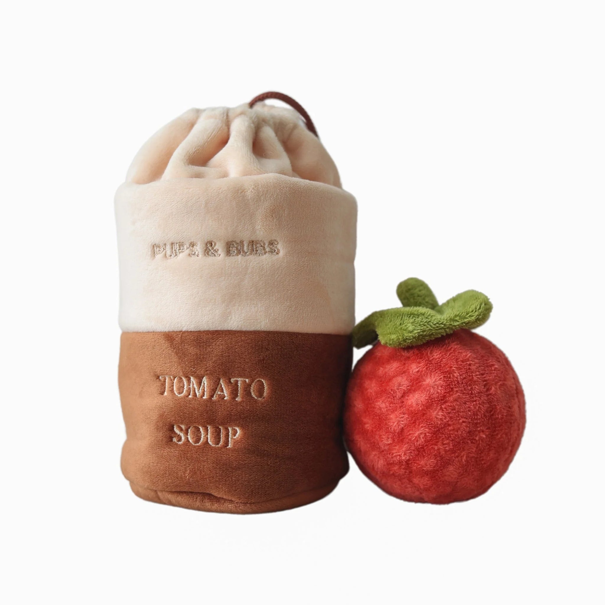 The complete interactive dog toy set featuring a brown and beige plush tomato soup can and a squeaky red tomato ball on a clean white background.