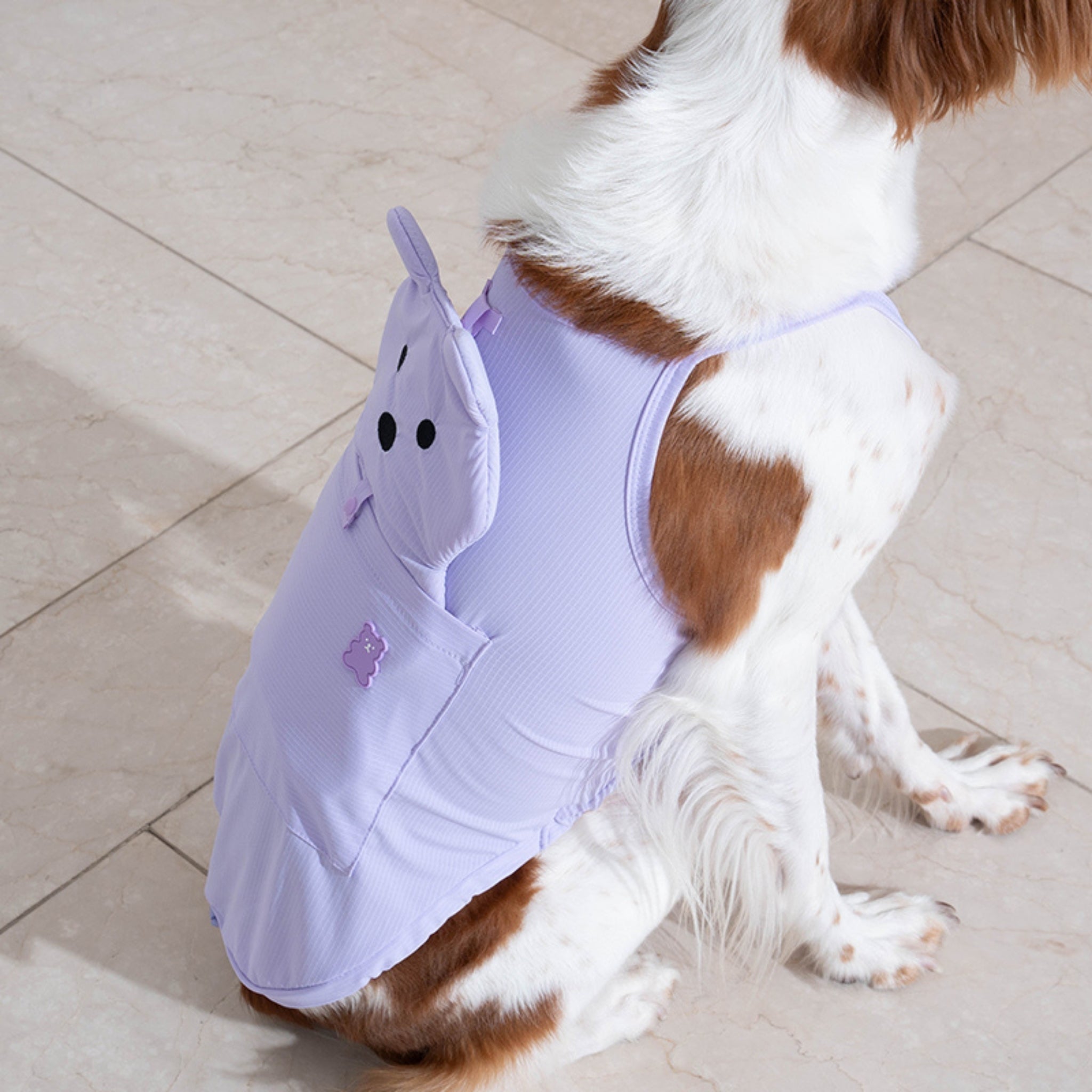 Close-up side view of a brown and white dog sitting down, highlighting the 3D bear head detail and functional back pocket of the lavender pet cooling shirt.
