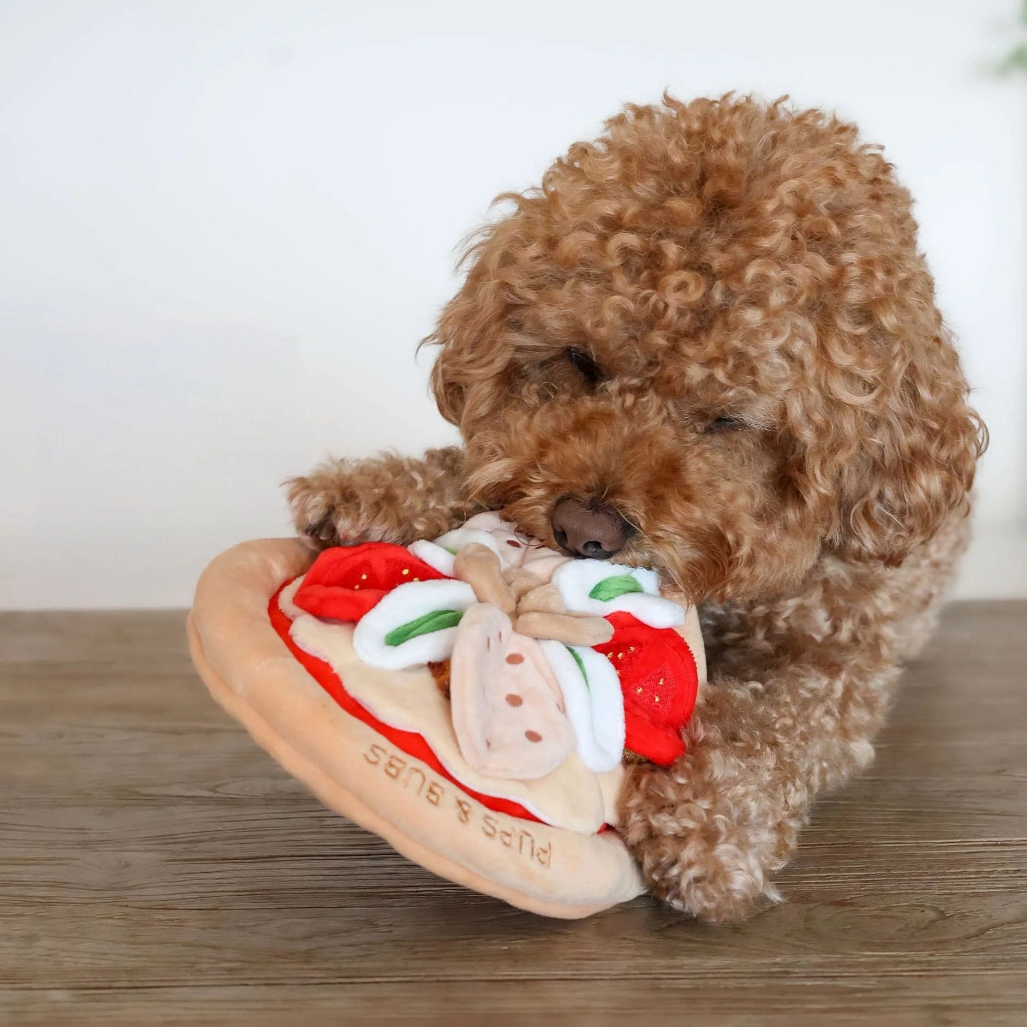 A cute poodle dog playing with the crinkly pizza snuffle mat on the floor, showcasing durable plush construction for pet mental stimulation.